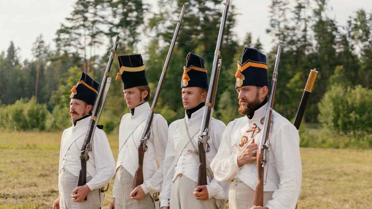 Four soldiers in historical uniforms stand in formation during a reenactment outdoors.